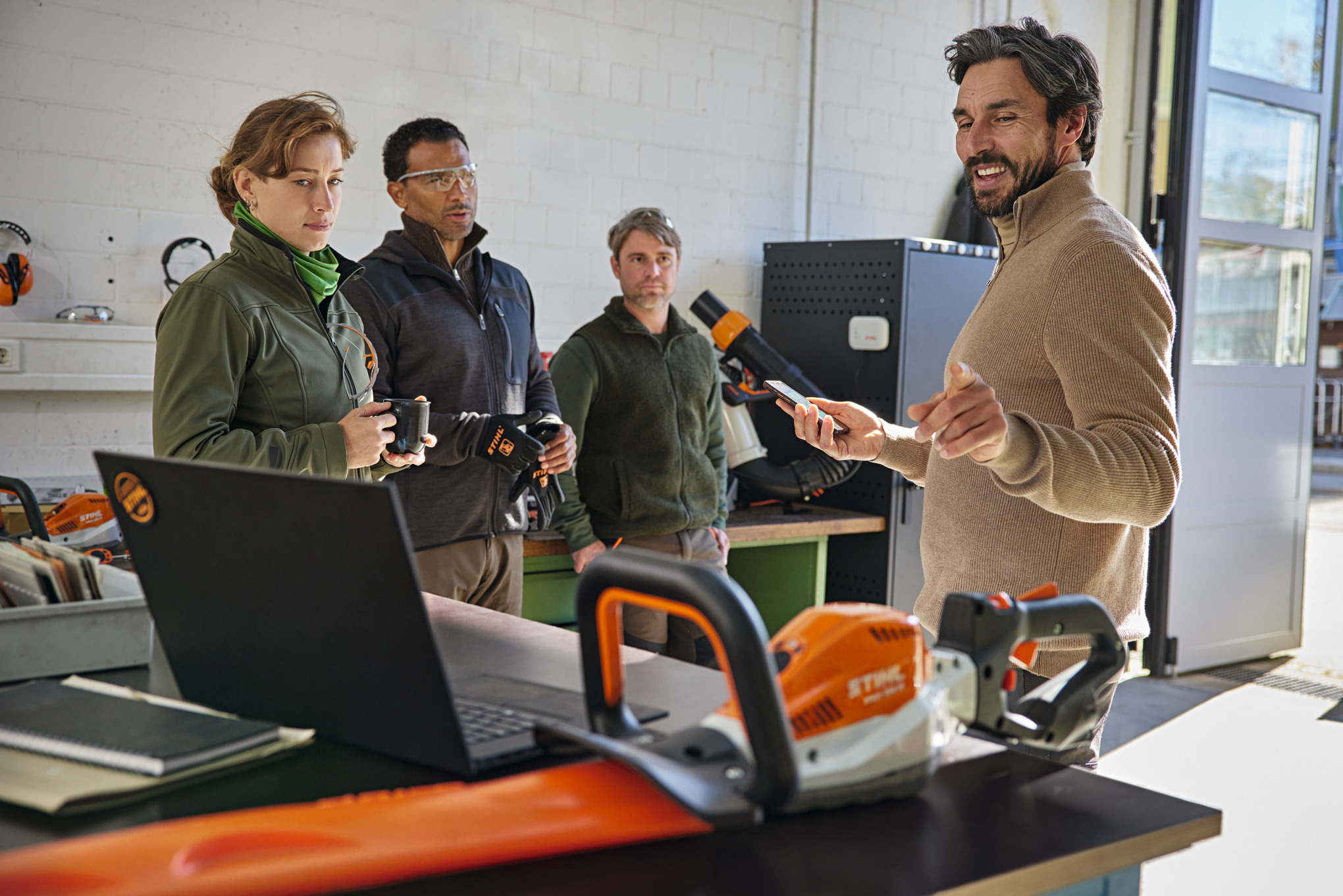 Quatro pessoas numa oficina e uma pessoa a explicar a aplicação STIHL connected num telemóvel